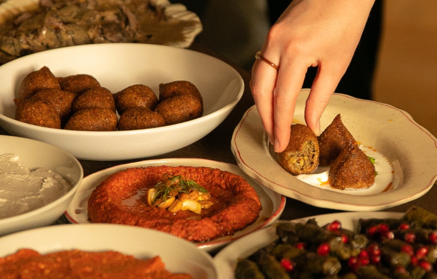 Guests reaching across a candlelit table laden with mezze — hummus, muhammara, stuffed vine leaves, falafel and saffron rice.