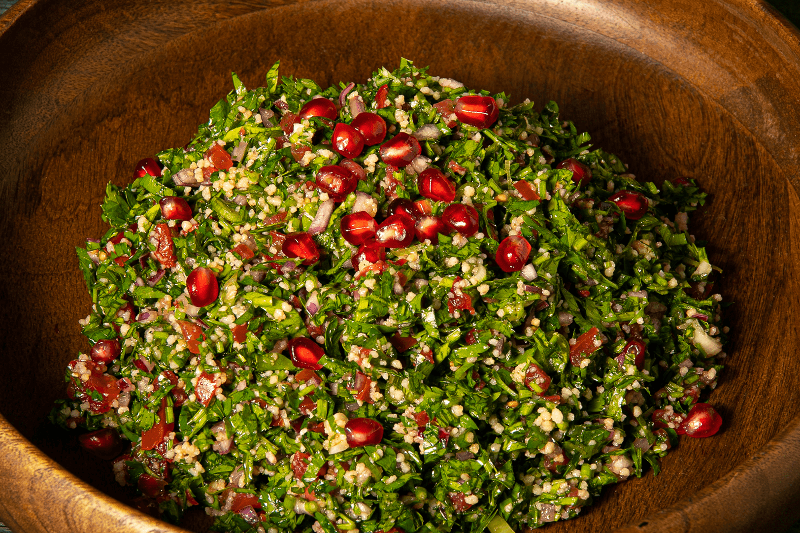 A generous wooden bowl of tabbouleh studded with pomegranate seeds, bulgur and finely chopped parsley.